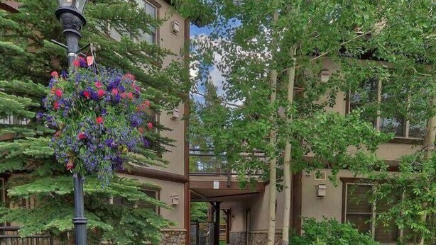 A pathway leading to a building entrance with a flower basket and greenery. - Corral Hideaway - Steps from Downtown! (Breckenridge)