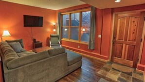 A living room with a sofa, a TV, a chair, and a wooden door. - Corral Hideaway - Steps from Downtown! (Breckenridge)