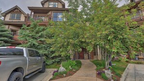 A two-story building with a stone facade, a covered porch, and a driveway leading to a gated entrance. - Corral Hideaway - Steps from Downtown! (Breckenridge)