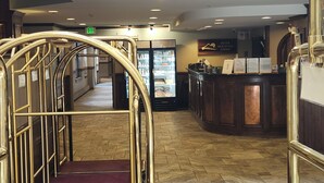 A hotel lobby with a marble floor, a reception desk, and a staircase with golden railings.