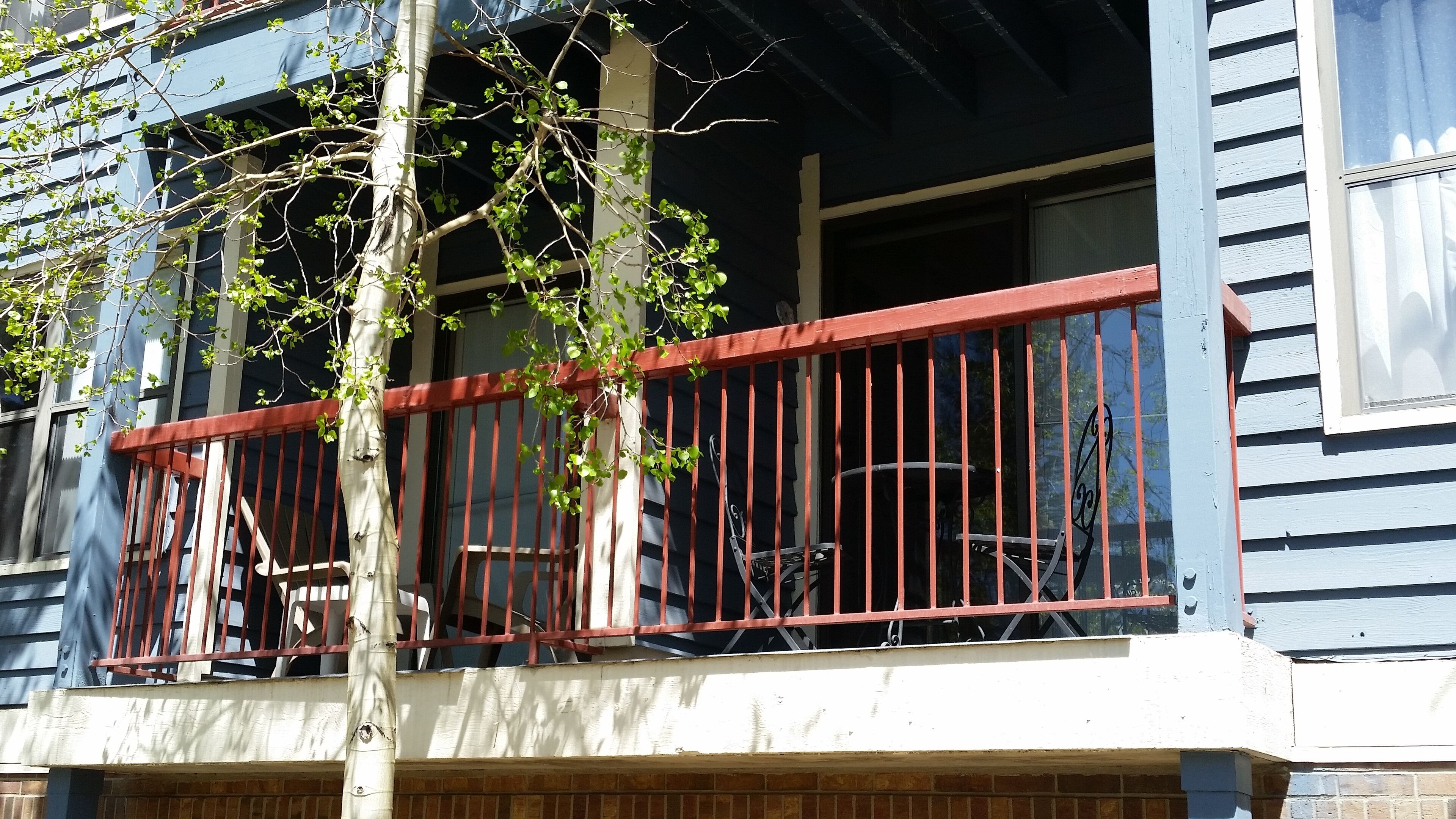 Een balkon met een rode balustrade, een boom en een stoel.