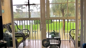 A room with a glass door leading to a balcony with outdoor furniture and a view of a green landscape. - Sunrise Dreamz - Steps from the Beach equipped with all you need! (Fort Pierce)