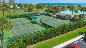 A tennis court with a net, surrounded by greenery and a building labeled "OCEAN VILLAGE". - Sunrise Dreamz - Steps from the Beach equipped with all you need! (Fort Pierce)