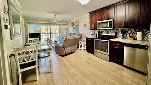 A modern kitchen with dark wooden cabinets, stainless steel appliances, and a dining area with a white table and chairs. - Sunrise Dreamz - Steps from the Beach equipped with all you need! (Fort Pierce)