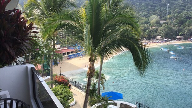 Ein Balkon mit Blick auf einen Strand, Palmen und ein klares, blaues Meer.