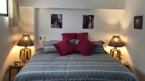 Ein Schlafzimmer mit einem Bett, zwei Wandleuchten, einem Deckenventilator und zwei abstrakten Bildern.