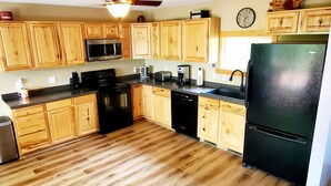A kitchen with wooden cabinets, a black refrigerator, a ceiling fan, and a clock on the wall. - Escape to Tranquility on Ross Lake: A Perfect Getaway! (Aitkin)