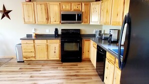 A kitchen with wooden cabinets, a black refrigerator, a microwave, and a stove. - Escape to Tranquility on Ross Lake: A Perfect Getaway! (Aitkin)