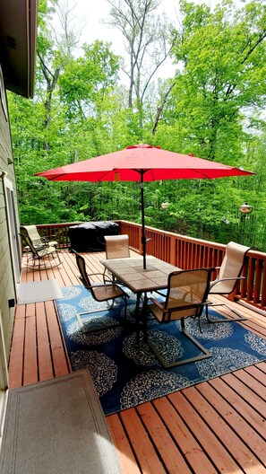 Una terraza con mobiliario exterior, un paraguas rojo y vistas a un follaje exuberante.