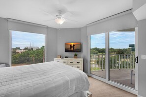 A bedroom with a large bed, a ceiling fan, a TV on the wall, and a balcony with a view of the city.