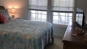 A bedroom with a bed, two windows with blinds, a ceiling fan, a bedside lamp, and a dresser with a mirror. - Tranquil Lakefront Setting near Clemson SC with Private, Covered Dock (Seneca)