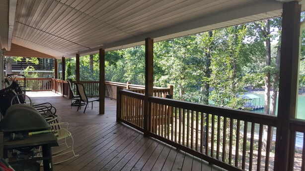 A covered outdoor deck with wooden railings, chairs, and tables. - Tranquil Lakefront Setting near Clemson SC with Private, Covered Dock (Seneca)