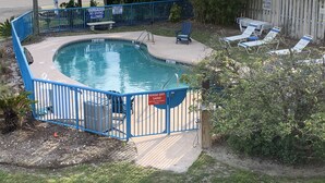 Piscina com cerca azul, cadeiras de descanso e placa indicando área rasa e proibição de mergulho.