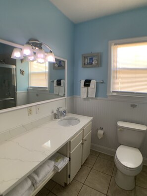 Une salle de bain avec un meuble-lavabo blanc, un évier, un miroir et des toilettes.