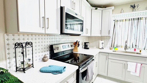 A kitchen with white cabinets, a black stove, a microwave, and a sink.