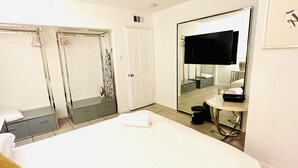 A hotel room with a bed, a desk with a chair, a mirror, and a wardrobe.