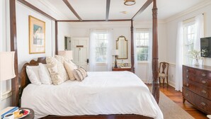 Un espacioso dormitorio con cama con dosel, cómoda de madera y un espejo grande.