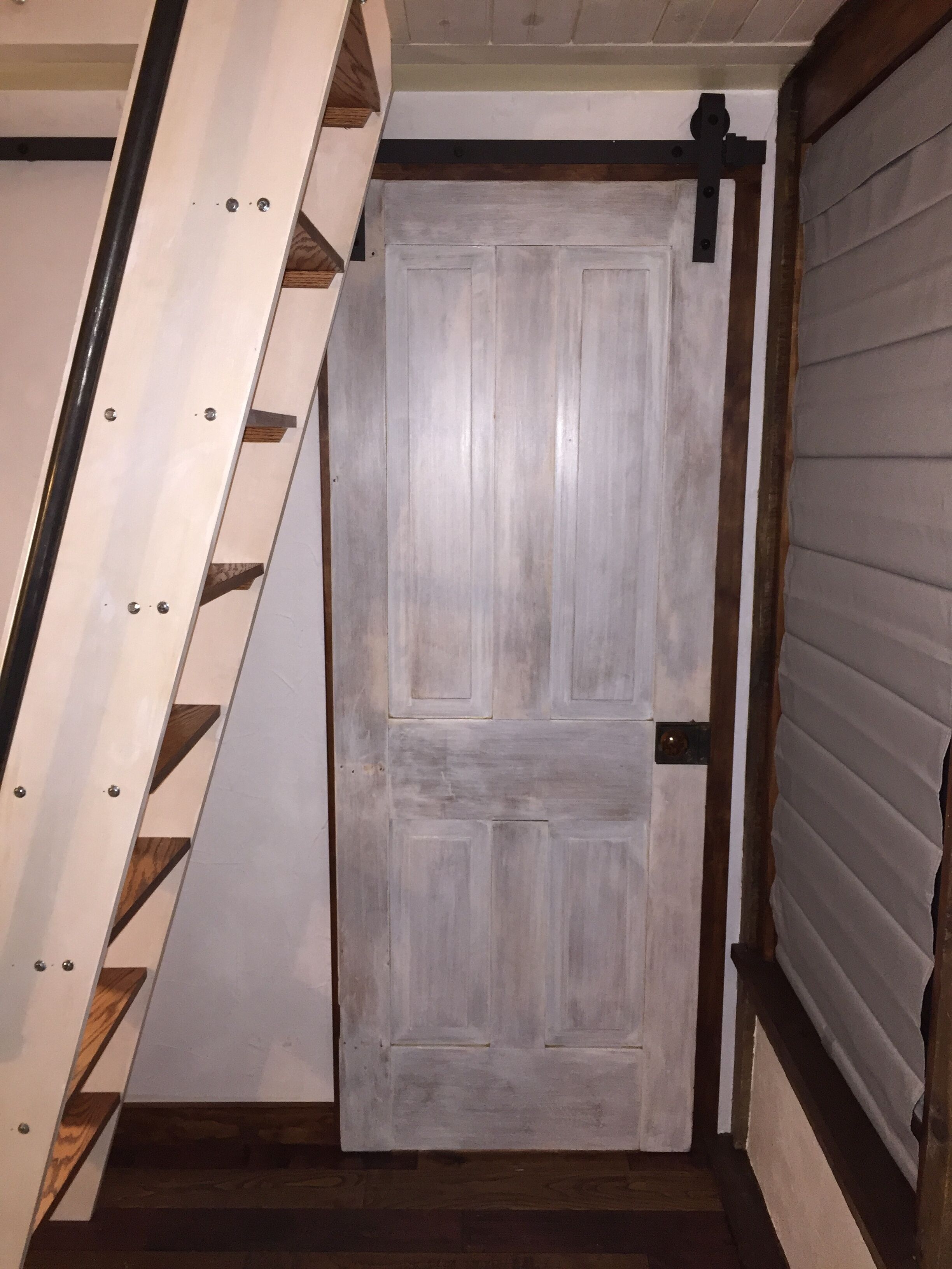 Eine Holztreppe führt zu einer weißen Tür mit einer Metallklinke.