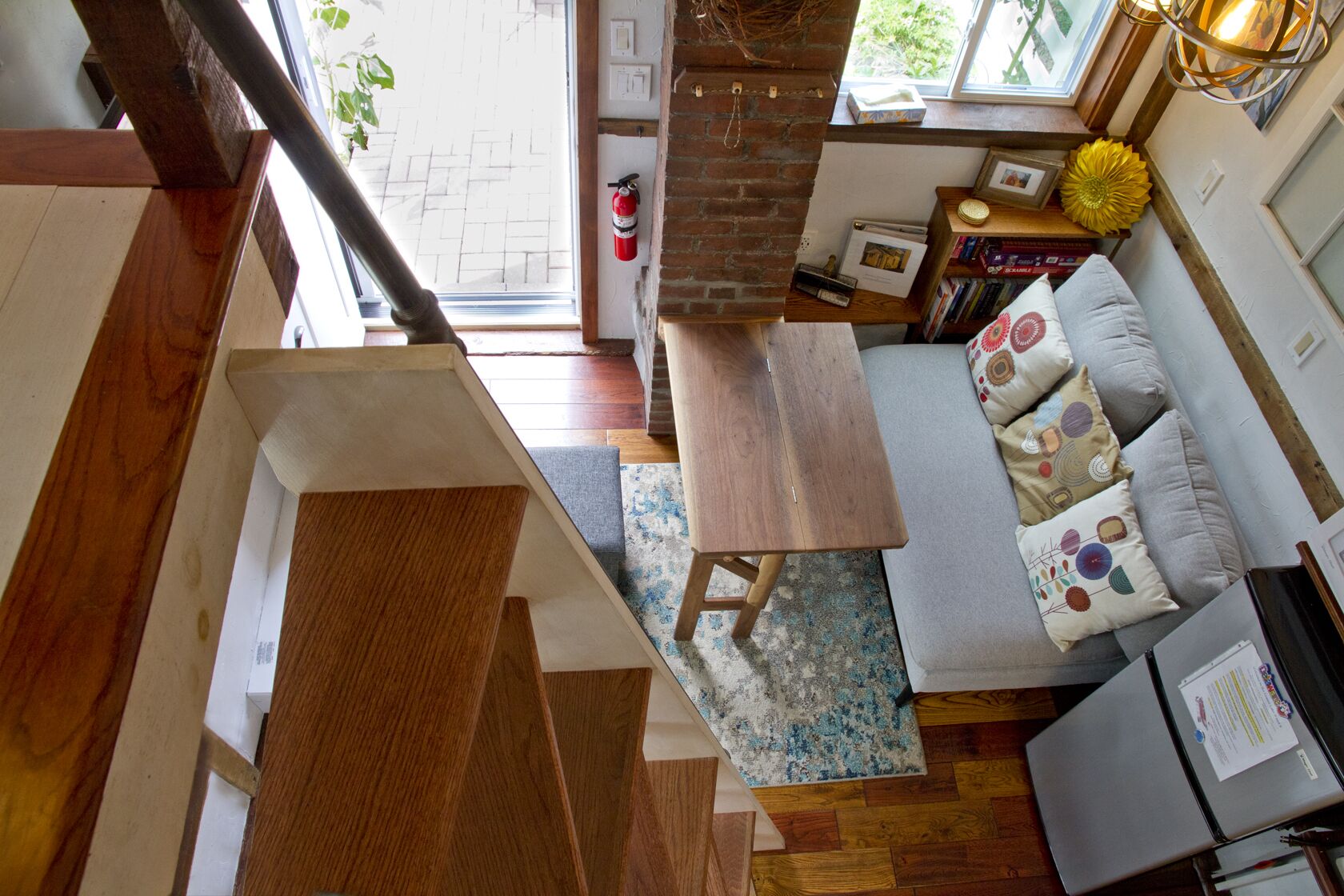 Une chambre moderne de style loft, avec un escalier en bois, un canapé agrémenté de coussins à motifs, une petite table en bois et une bibliothèque.