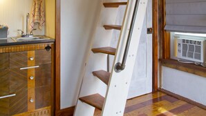 Un espai tipus loft amb una escala de fusta, zona de cuina i una finestra gran.
