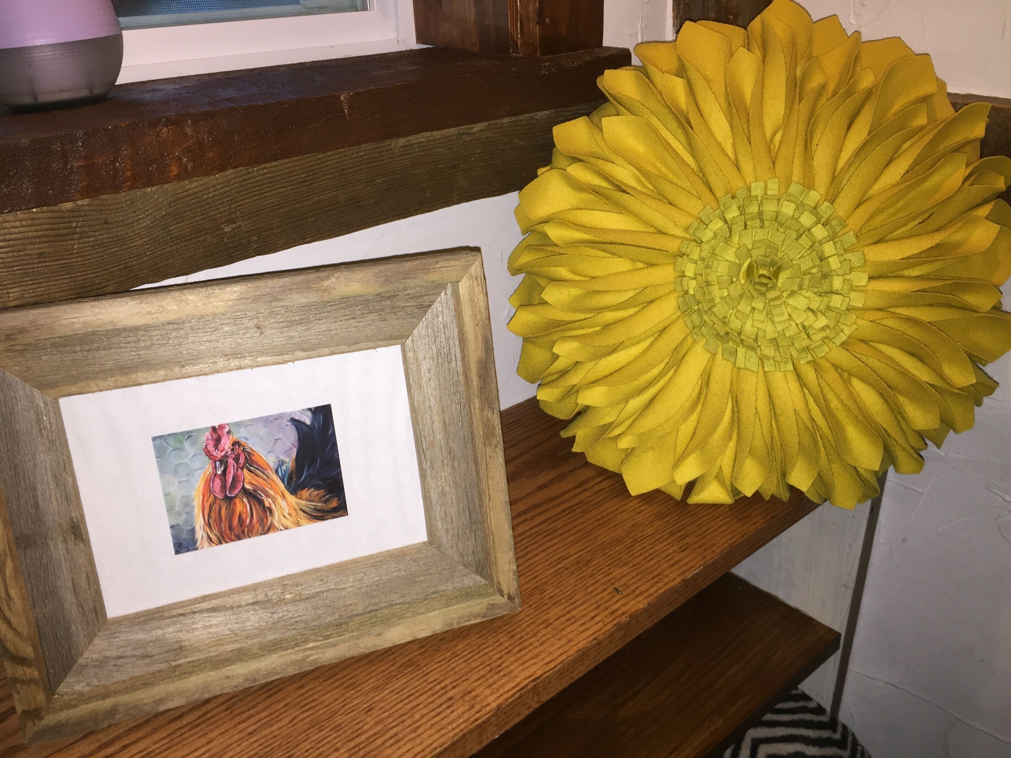 A wooden shelf with a framed picture and a large yellow sunflower decoration.