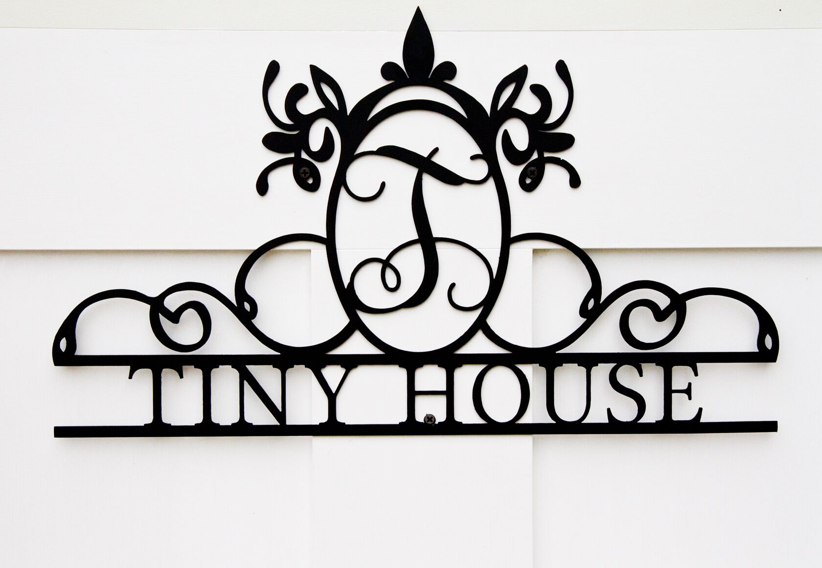 Een metalen bord met de tekst 'TINY HOUSE' en een decoratief ontwerp erboven.