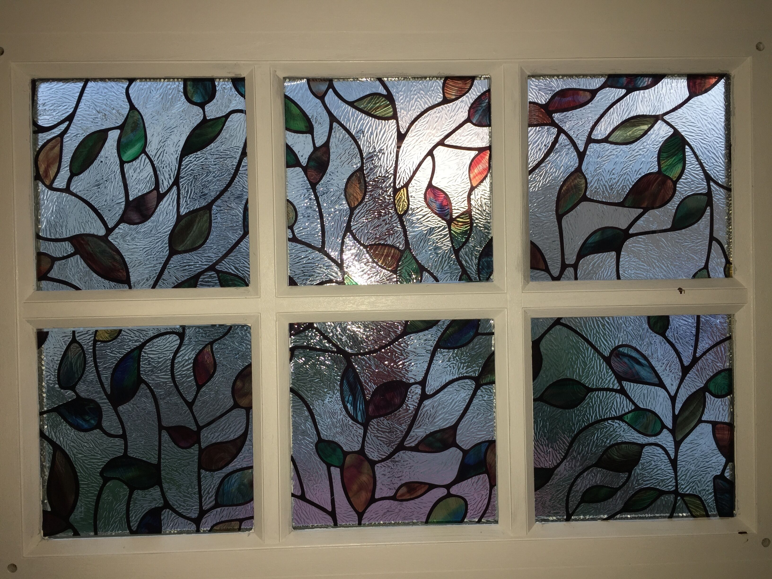 Una ventana con seis cristales, cada uno con un diseño de vitral con motivos de hojas.