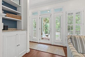 A room with white cabinetry, a striped sofa, and a view through a door with shutters.