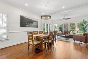 A spacious dining area with a wooden table and chairs, a ceiling fan, and a large window with a view of greenery.
