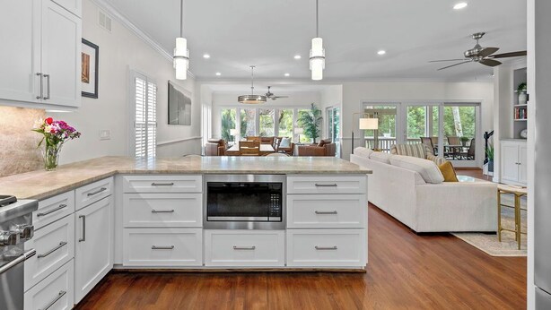 A modern kitchen with white cabinetry, a central island with a microwave, pendant lighting, and a view to a living area with a sofa and a dining table. - Fabulous 4 BR/3.5 BA w/ Golf Views! Close to Beach! Amenity access included! No Pets Allowed. (Seabrook Island)