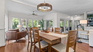 A dining area with a wooden table and chairs, a ceiling fan, and large windows with a view of greenery. - Fabulous 4 BR/3.5 BA w/ Golf Views! Close to Beach! Amenity access included! No Pets Allowed. (Seabrook Island)