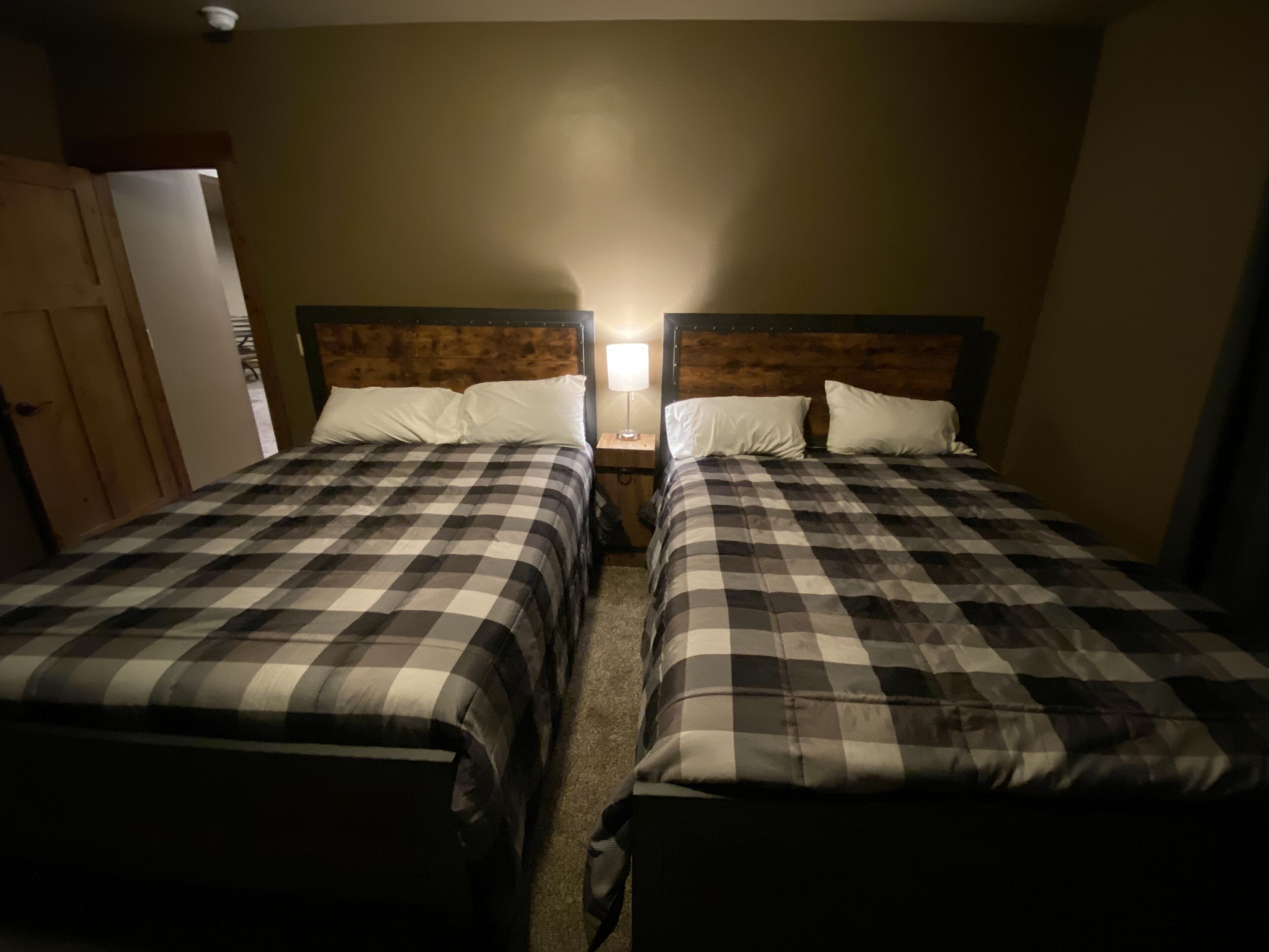 Una habitación con dos camas, cada una con una colcha a cuadros y almohadas blancas. Entre las camas hay una mesita de noche con una lámpara.