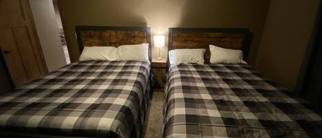 Una habitación con dos camas, cada una con una colcha a cuadros y almohadas blancas. Entre las camas hay una mesita de noche con una lámpara.