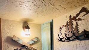 A room with textured walls, a wooden chair with a colorful cushion, a wall-mounted light fixture, and a decorative wooden piece with a mountain design. - Quiet Retreat with private courtyard In Grand Lake Village! (Grand Lake)
