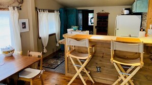 A cozy kitchen with wooden walls, a dining table with chairs, and a refrigerator. - Quiet Retreat with private courtyard In Grand Lake Village! (Grand Lake)