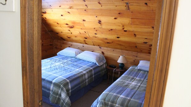 Une chambre avec deux lits, des murs en bois, une petite table avec une lampe et une porte.