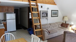 Une pièce de style loft avec une échelle en bois, un coin cuisine, un canapé et un espace repas.