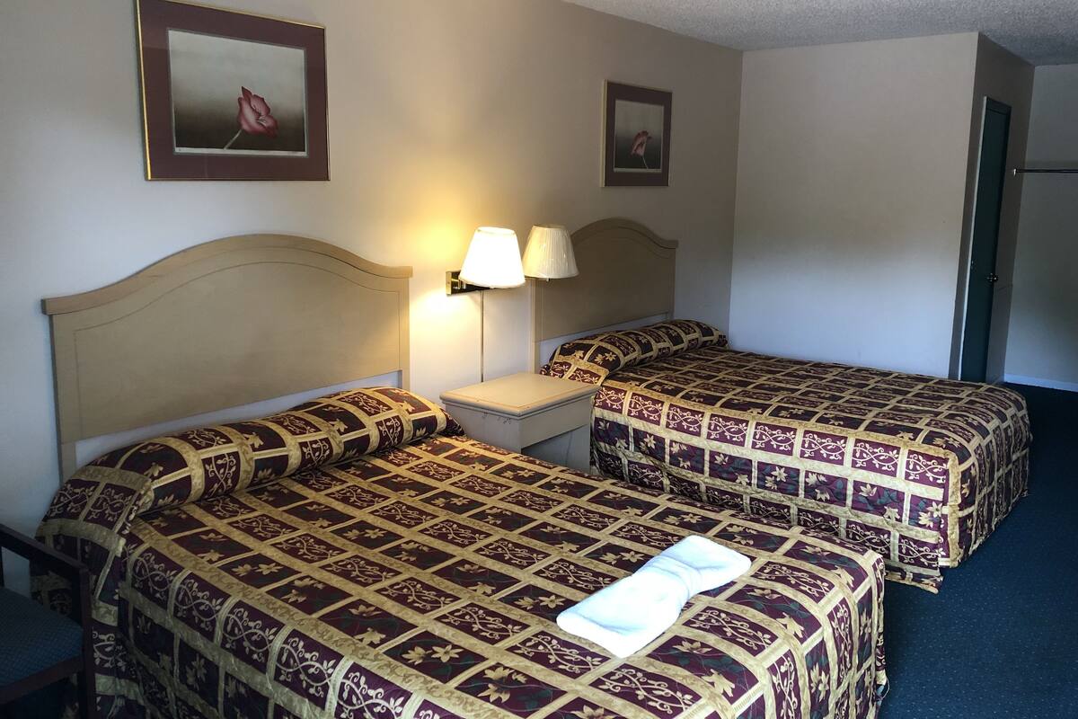 A hotel room with two beds, a nightstand, a lamp, and two framed pictures on the wall.
