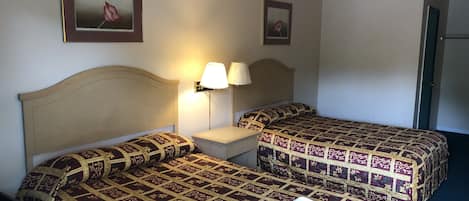 A hotel room with two beds, a nightstand, a lamp, and two framed pictures on the wall.