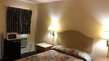 Een hotelkamer met een bed, een magnetron, een kachel, een nachtkastje en een lamp.