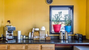 A kitchen with a coffee machine, various containers, and a window with potted plants. - Relax Inn (Lewisburg)
