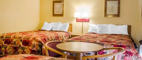 A hotel room with two beds, a round table, and two wall-mounted lamps.