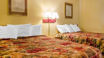 A hotel room with two beds, each with white pillows and a colorful quilted bedspread. There is a nightstand with a lamp between the beds.