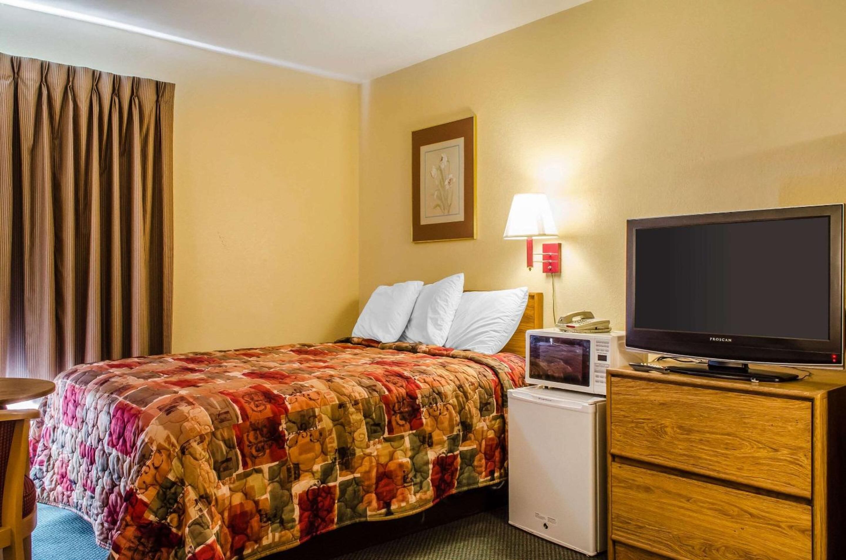 Een hotelkamer met een bed, een televisie, een magnetron en een houten dressoir.