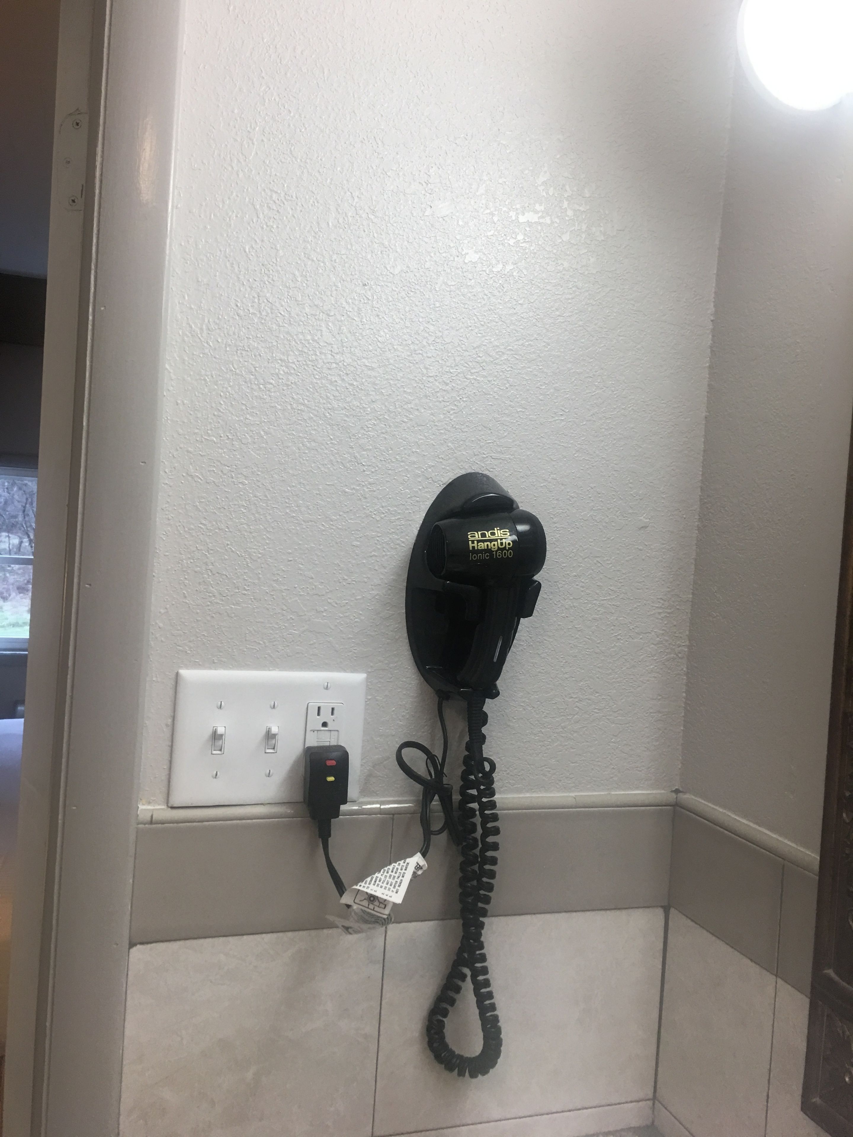 Een zwarte telefoon bevestigd aan een gestructureerde muur, verbonden met een stopcontact via een kabel.