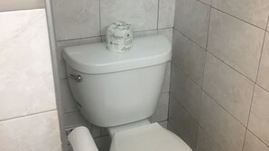 A small, compact bathroom with a white toilet, a toilet paper holder, and a roll of toilet paper.