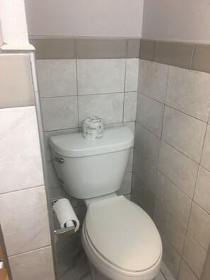 A small, compact bathroom with a white toilet, a toilet paper holder, and a roll of toilet paper.