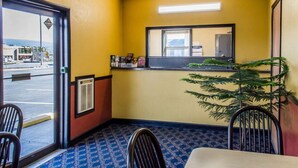 A small, brightly lit room with yellow walls, a large mirror, and a potted plant. There are two chairs and a table, with a window showing a street view. - Relax Inn (Lewisburg)