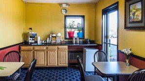 A small, yellow-walled room with a kitchenette, a window with potted plants, and a dining area with wooden chairs and tables. - Relax Inn (Lewisburg)
