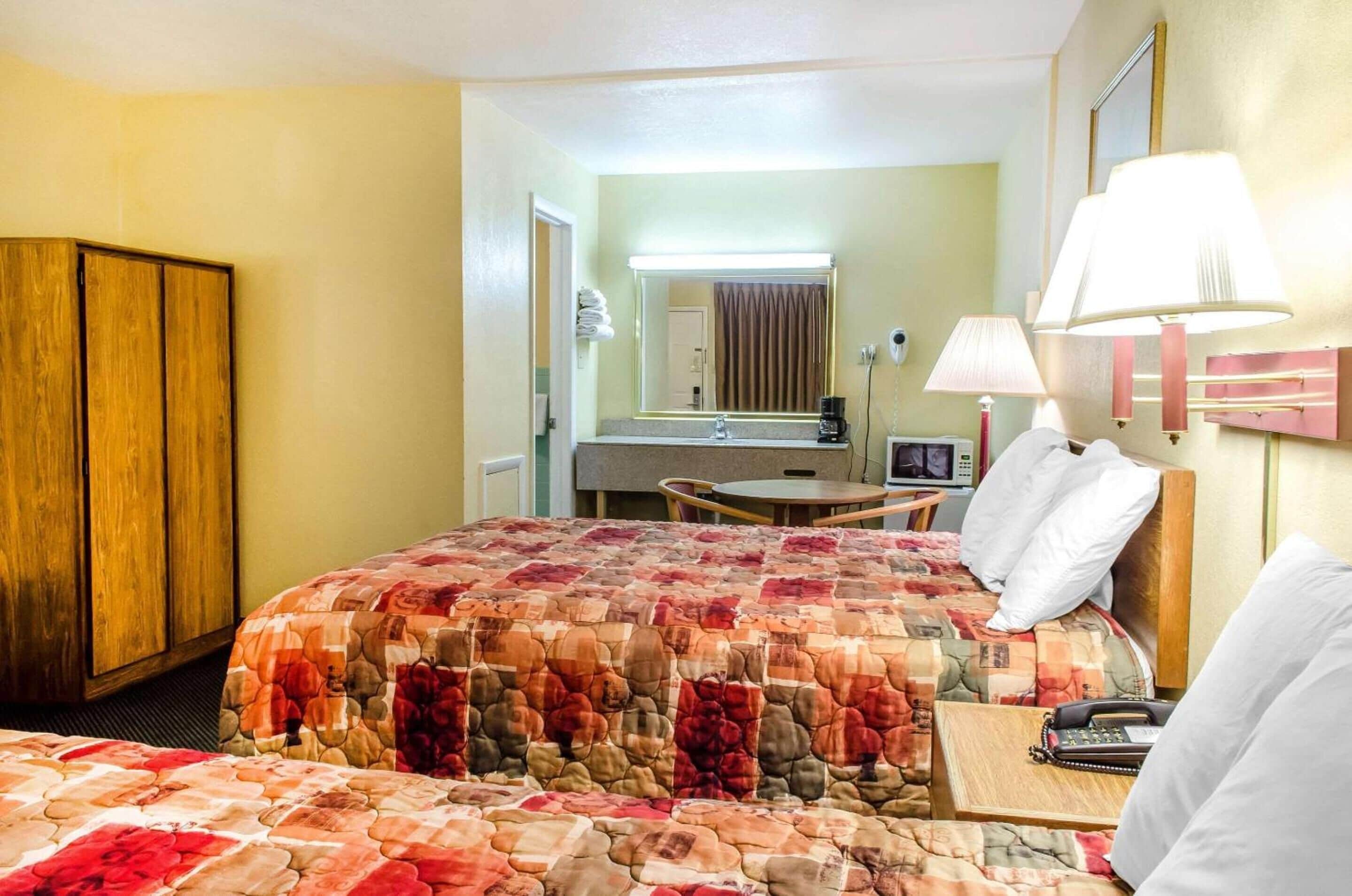 A hotel room with a large bed, a desk with a chair, a small table, a mirror, and a lamp.